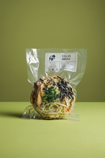 Packaged Frozen Vegan Shoyu Ramen in a clear plastic wrapping with visible toppings such as ground tofu, mushrooms, and scallions, against a brick wall background.
